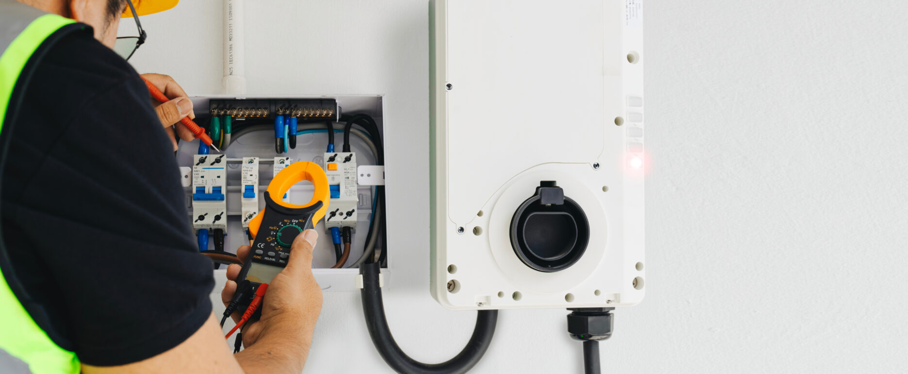 Electrician tests wiring with a clamp meter during home EV charger installation, ensuring safety and precision.