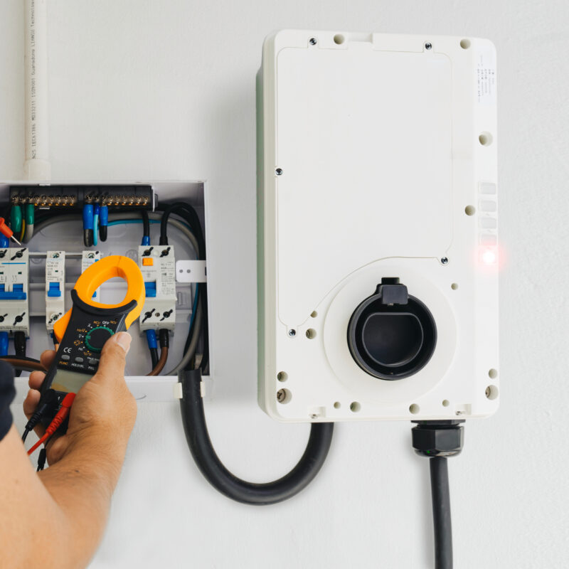 Electrician tests wiring with a clamp meter during home EV charger installation, ensuring safety and precision.
