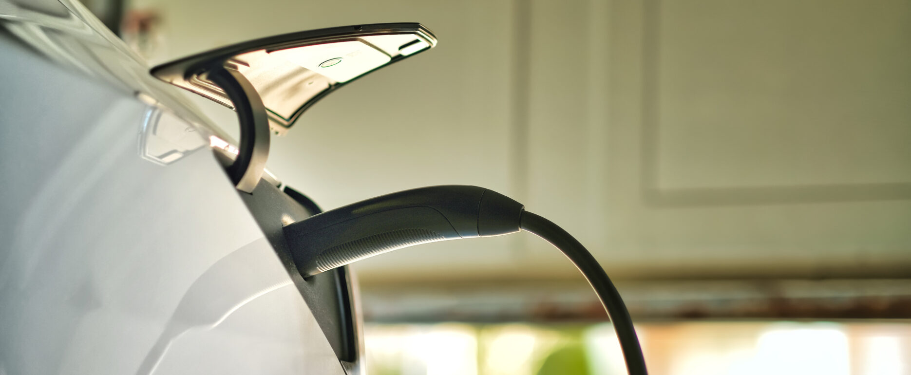 A white electric vehicle charges in a garage, connected to a home EV charger.