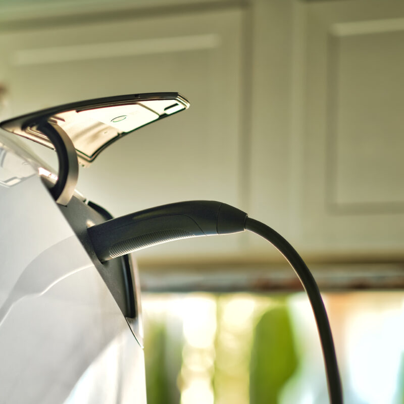 A white electric vehicle charges in a garage, connected to a home EV charger.